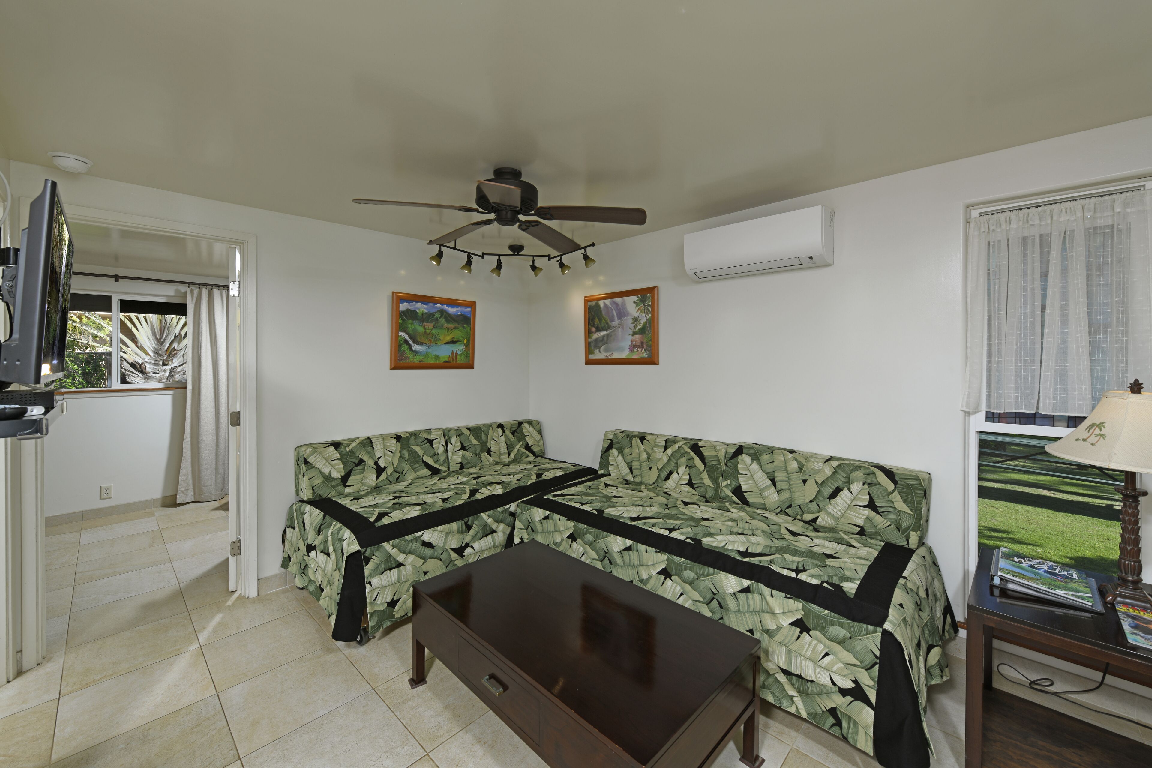 A living room with a sofa, a coffee table, a ceiling fan, and two wall-mounted paintings.