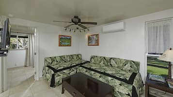 A living room with a sofa, a coffee table, a ceiling fan, and two wall-mounted paintings.