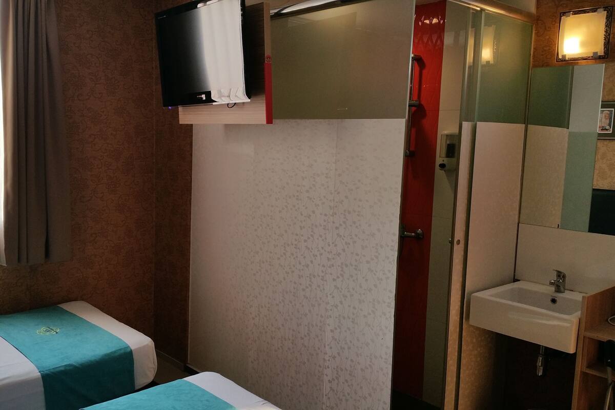 Ein Hotelzimmer mit zwei Betten, einer Dusche, einem Waschbecken und einem Fernseher.