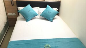 A neatly made bed with two teal pillows and a teal bedspread, featuring a logo. - ST Signature Bugis Beach (Singapore)