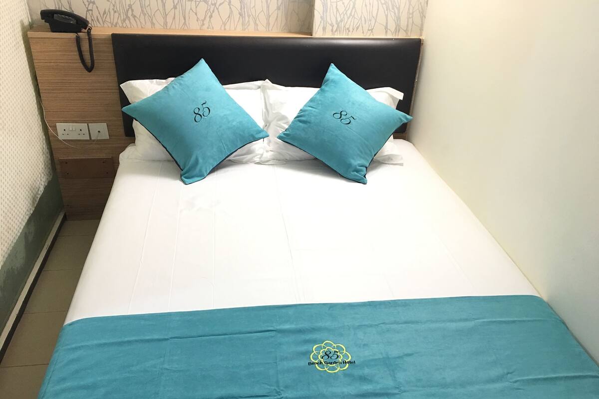 Ein ordentlich bezogenes Bett mit zwei türkisfarbenen Kissen und einer türkisfarbenen Bettdecke, mit einem Logo.