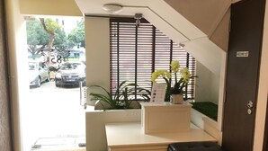 A reception area with a desk, a black cushioned bench, a potted plant, and a window with blinds. - ST Signature Bugis Beach (Singapore)