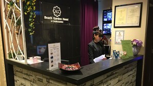 A reception desk at the Beach Garden Hotel with a black counter, a floral decoration, a framed certificate, and a menu stand. - ST Signature Bugis Beach (Singapore)