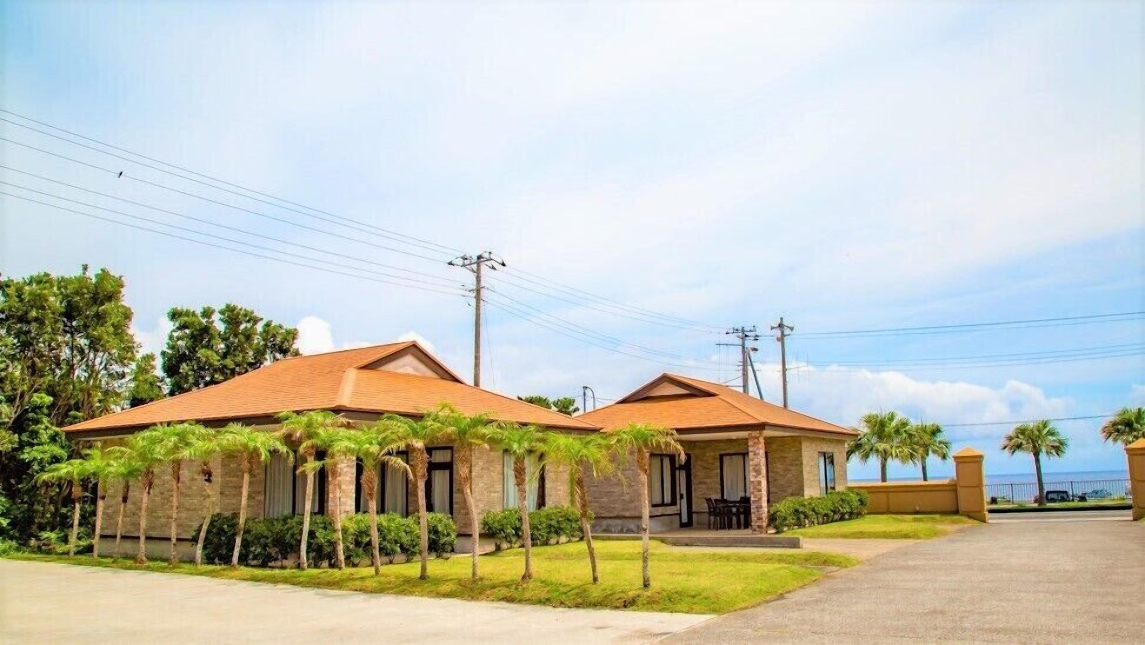 Two buildings with a flat roof, surrounded by palm trees and a clear sky.