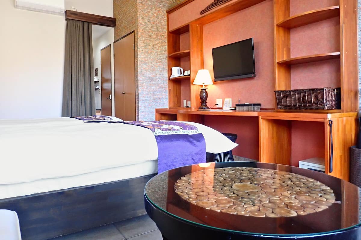 A hotel room with a bed, a desk with a lamp, a television, and a decorative wall.