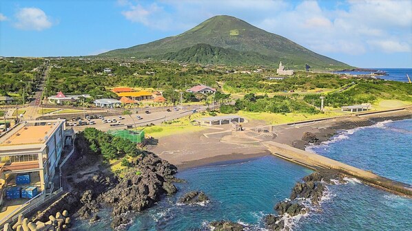 Une ville côtière, avec une montagne imposante en arrière-plan, une plage au rivage rocheux et une route menant à un parking.