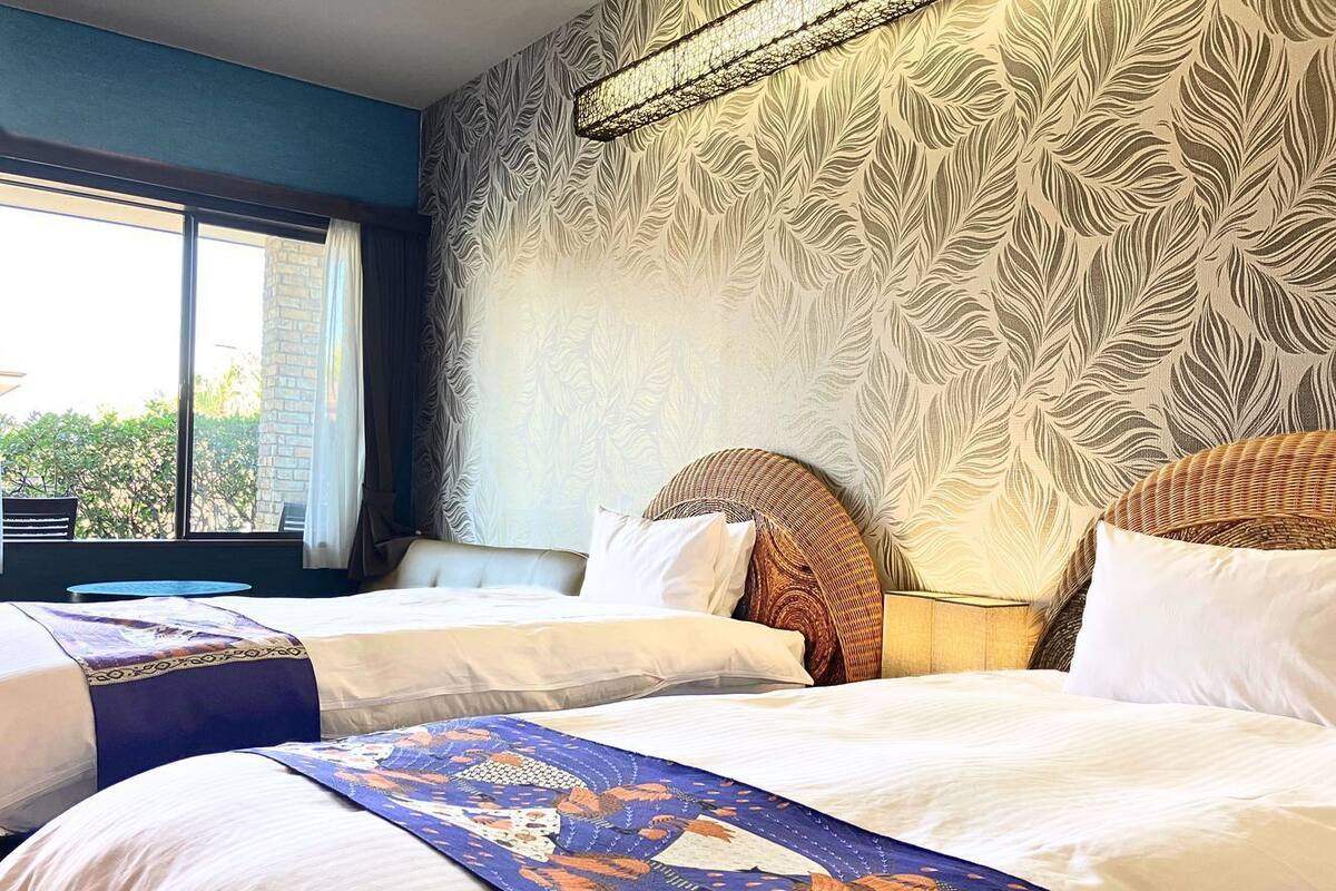 A hotel room with two beds, a large window, and a patterned wall.