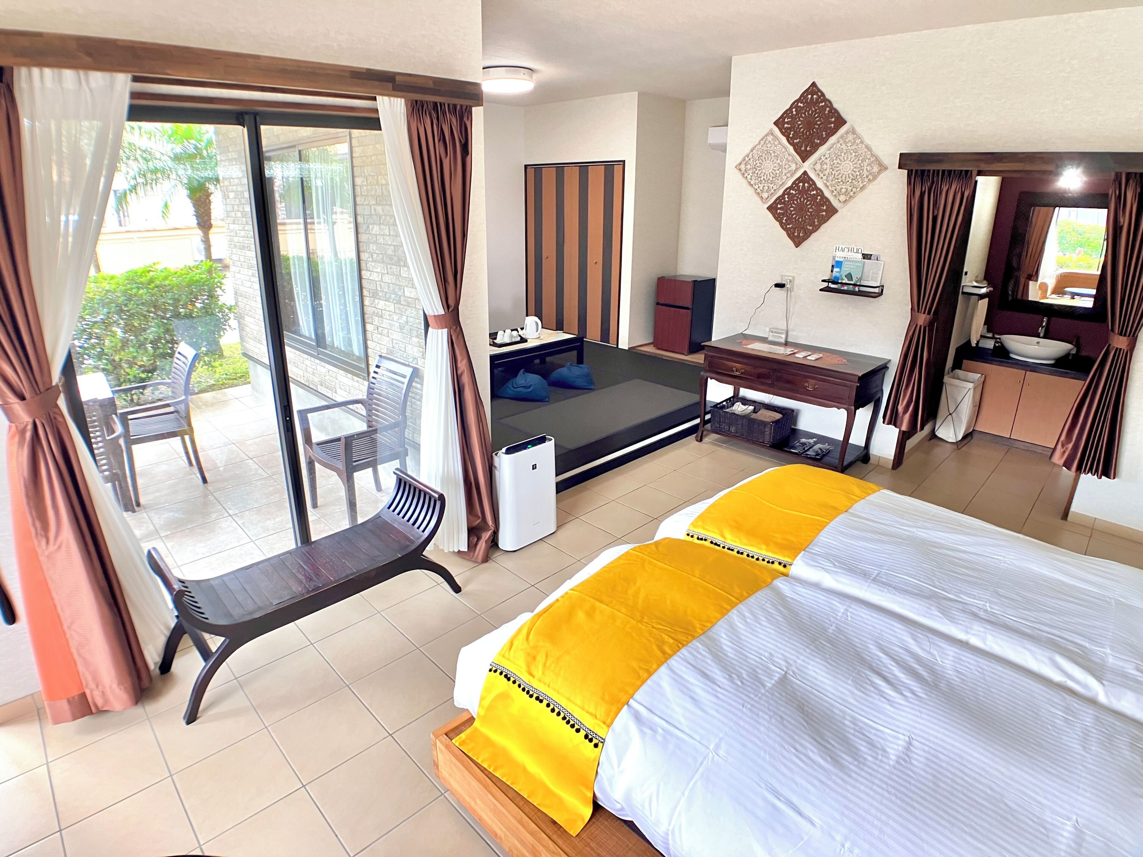 Habitación de hotel con cama, escritorio, silla, mesita, lavamanos y balcón con sillas.
