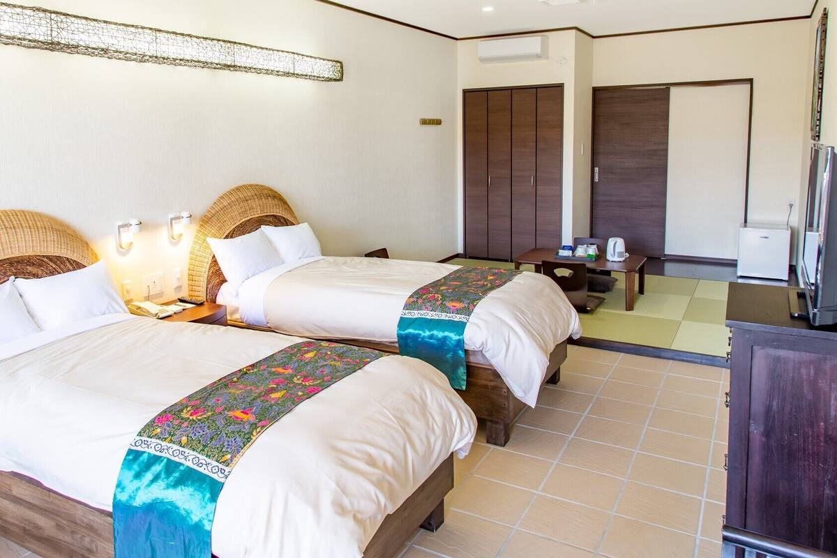 A hotel room with two beds, a television, a minibar, and a large mirror.