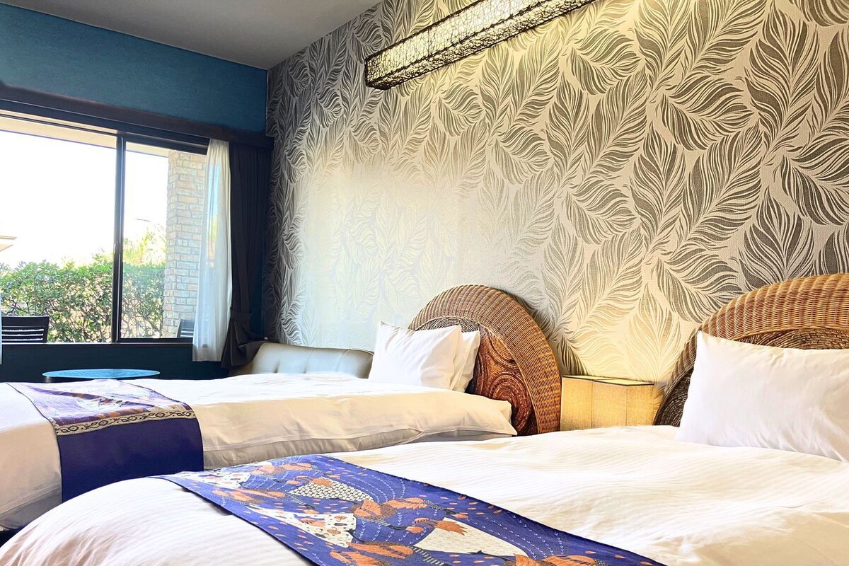 A hotel room with two beds, a large window, and a patterned wall.