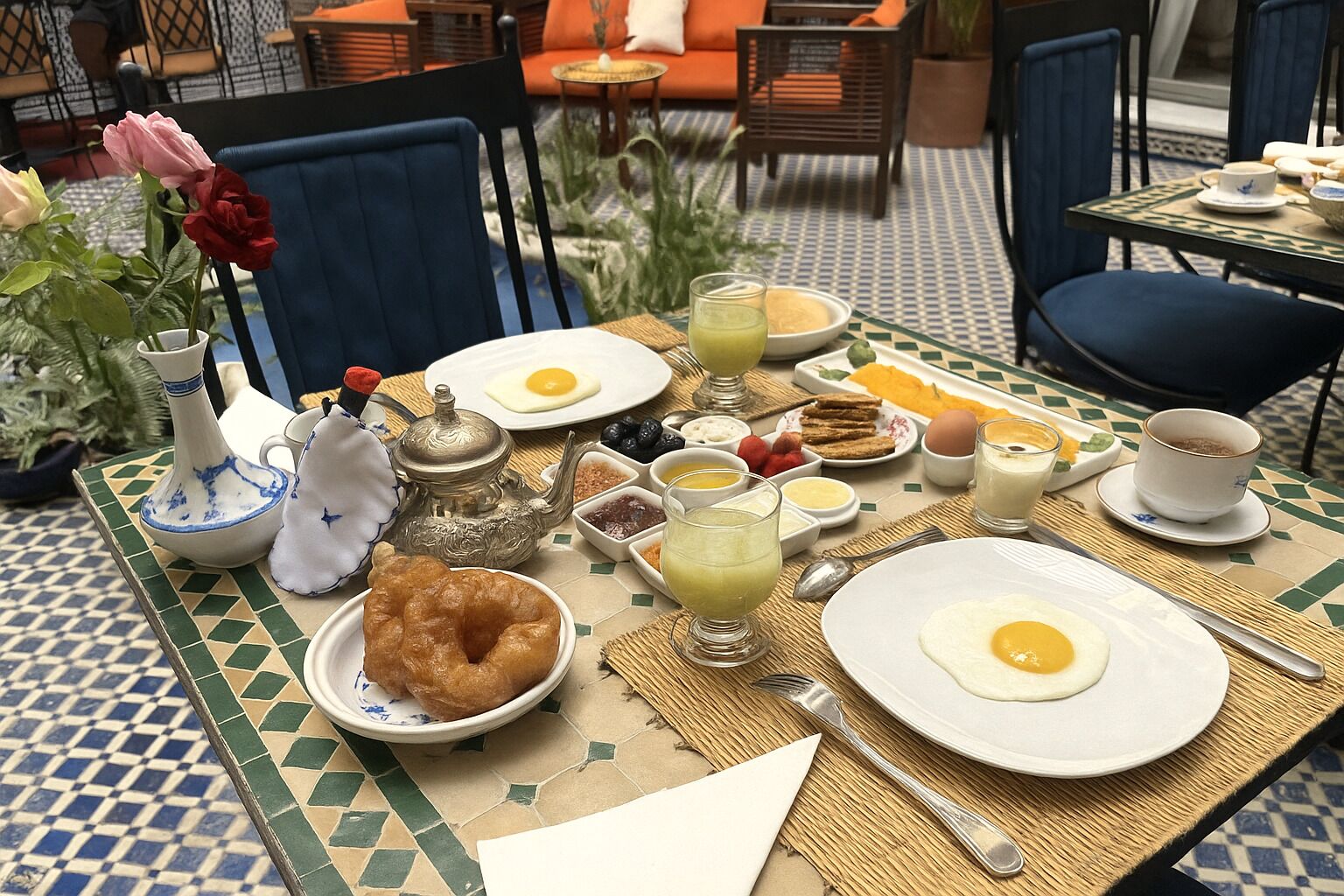 Una mesa de desayuno con platos de huevos, tostadas y fruta, junto con diferentes condimentos y un hervidor de té.