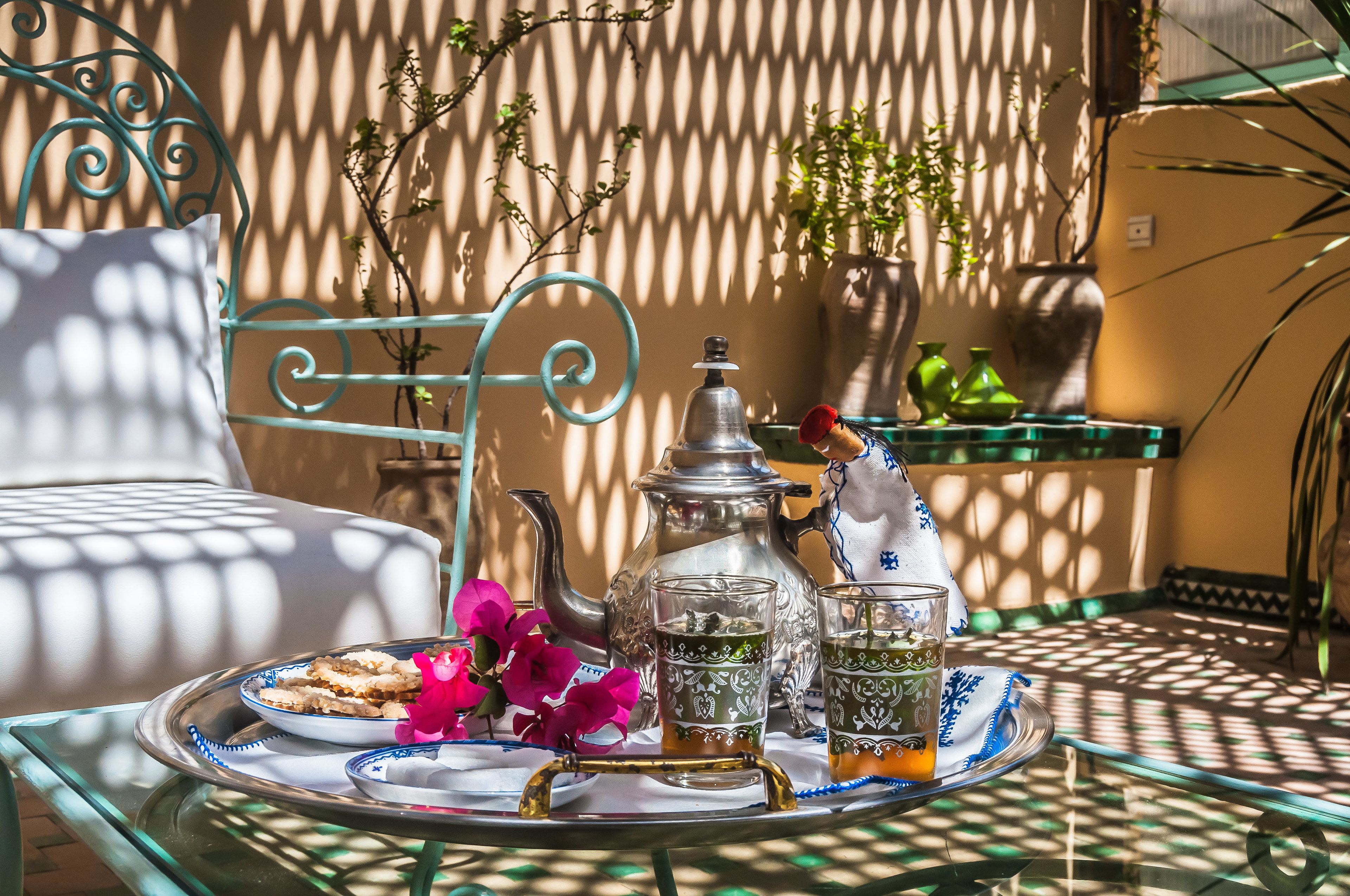A breakfast setup with a tray, teapot, glasses, and pastries on a table with a metal frame.