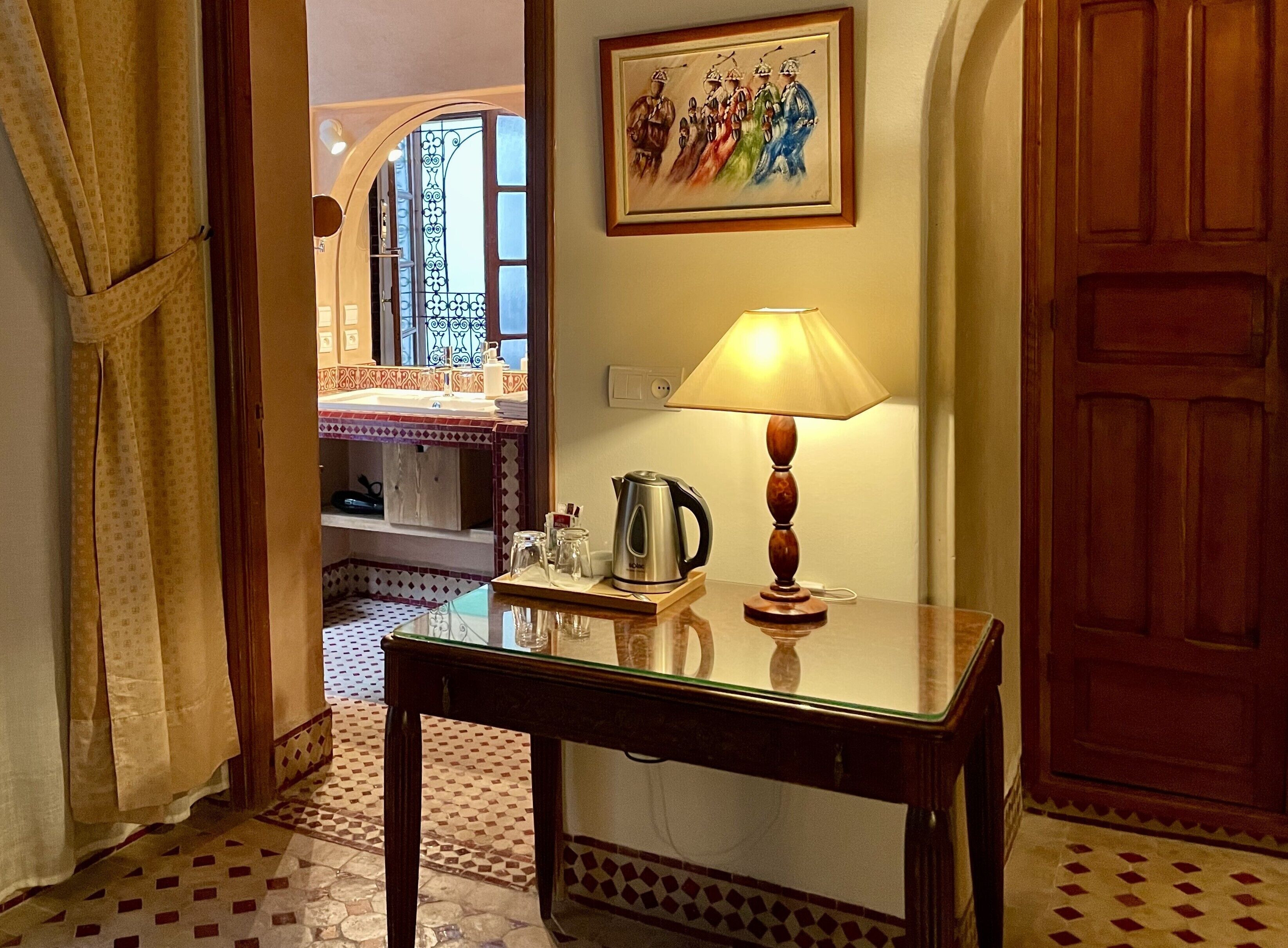 A room with a table, a lamp, a kettle, and a painting on the wall.