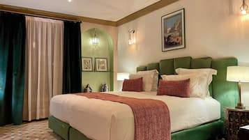 Quarto de hotel com uma cama grande, cabeceira estofada em verde, lençóis brancos e um tapete com padrão verde e branco.