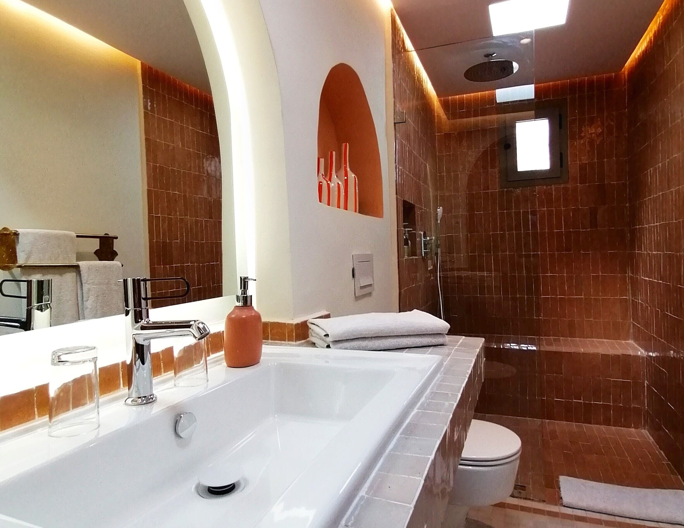 Une salle de bain avec un grand lavabo blanc, un miroir, une douche et des toilettes.