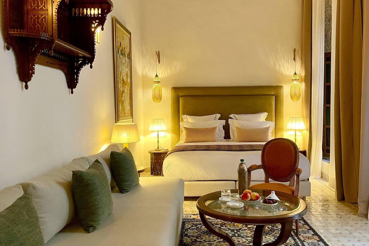 A hotel room with a bed, a sofa, a table with fruits, and two lamps.