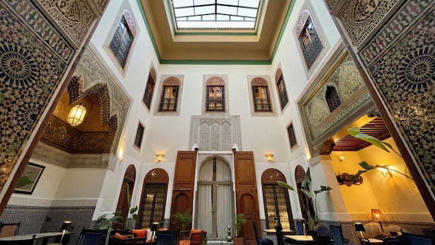 Un interior espacioso con techo alto, diseños ornamentales en las paredes y un área central abierta con mesas y sillas.