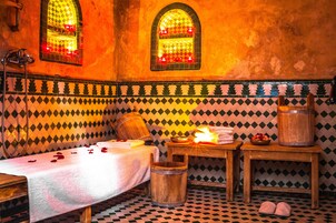 Um quarto com uma cama, um balde de madeira, uma mesa com toalhas e um recipiente grande para água.