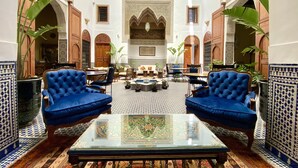 Un hall amplio con techos altos, arcos ornamentales y una zona de estar central con sillones tapizados en azul y una mesa con superficie de vidrio.