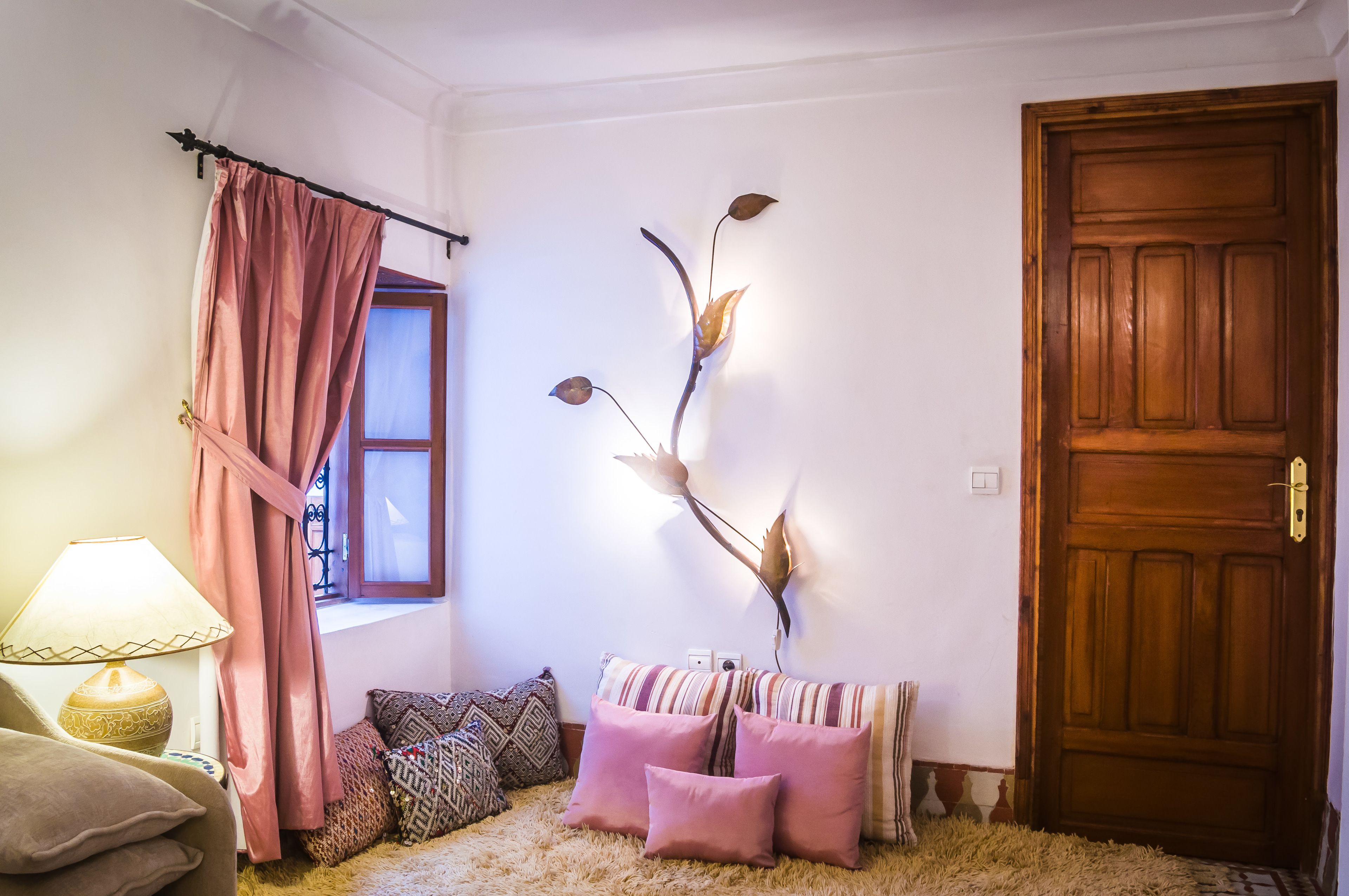 Une pièce chaleureuse avec une porte en bois, une fenêtre avec des rideaux, un canapé agrémenté de coussins à motifs et une branche décorative accrochée au mur.