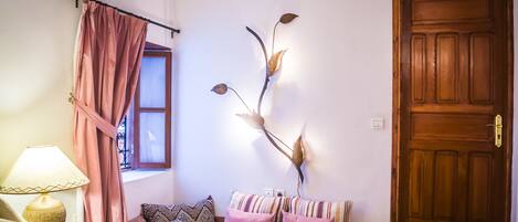Une pièce chaleureuse avec une porte en bois, une fenêtre avec des rideaux, un canapé agrémenté de coussins à motifs et une branche décorative accrochée au mur.