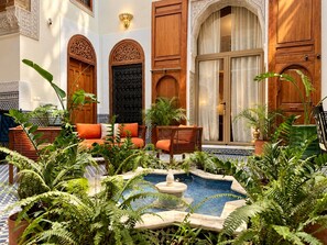 A courtyard with a fountain, seating area, and ornate doors.