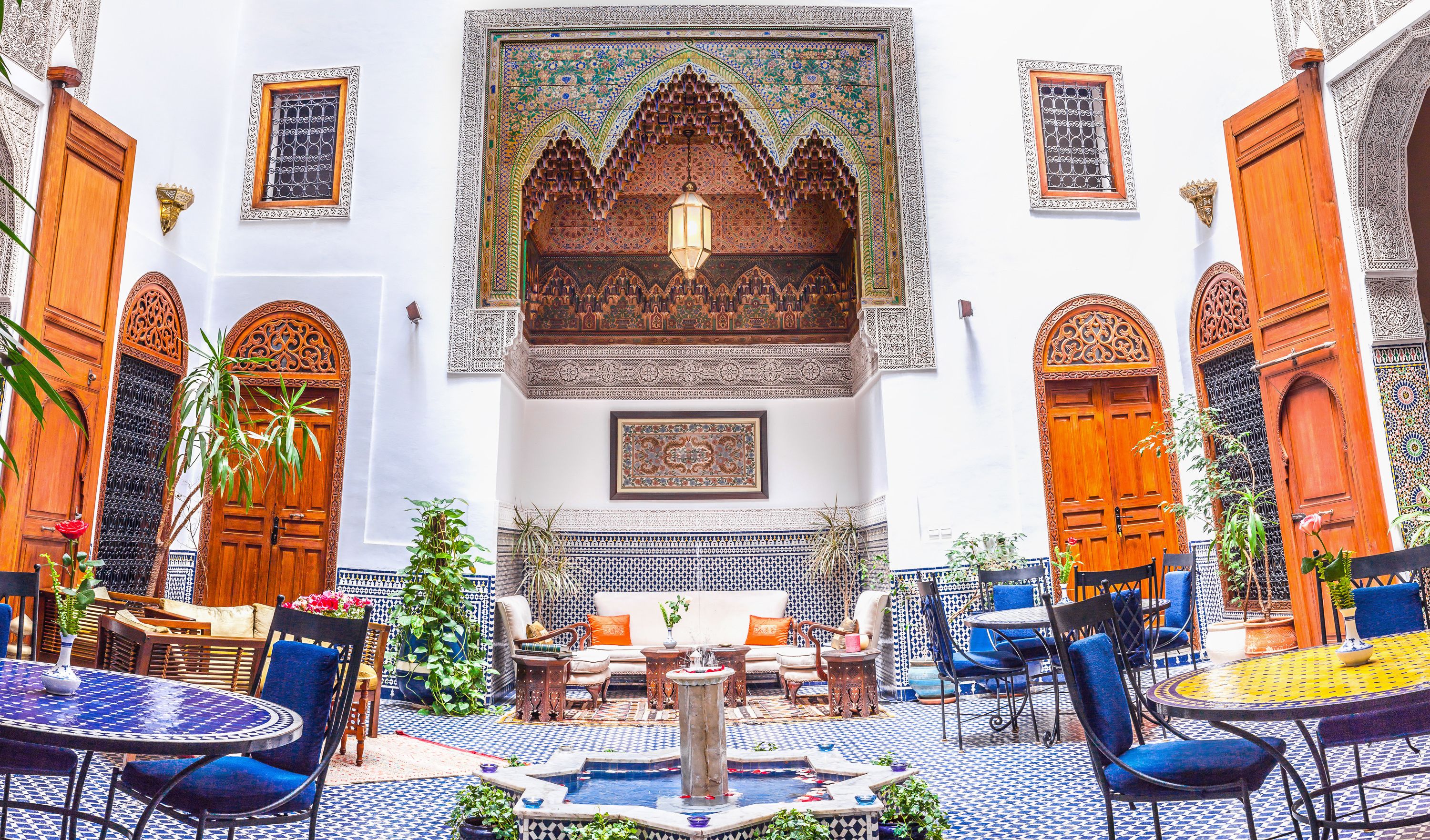 Un patio interior con puertas de madera ornamentadas, una fuente central y suelo de baldosas estampadas.