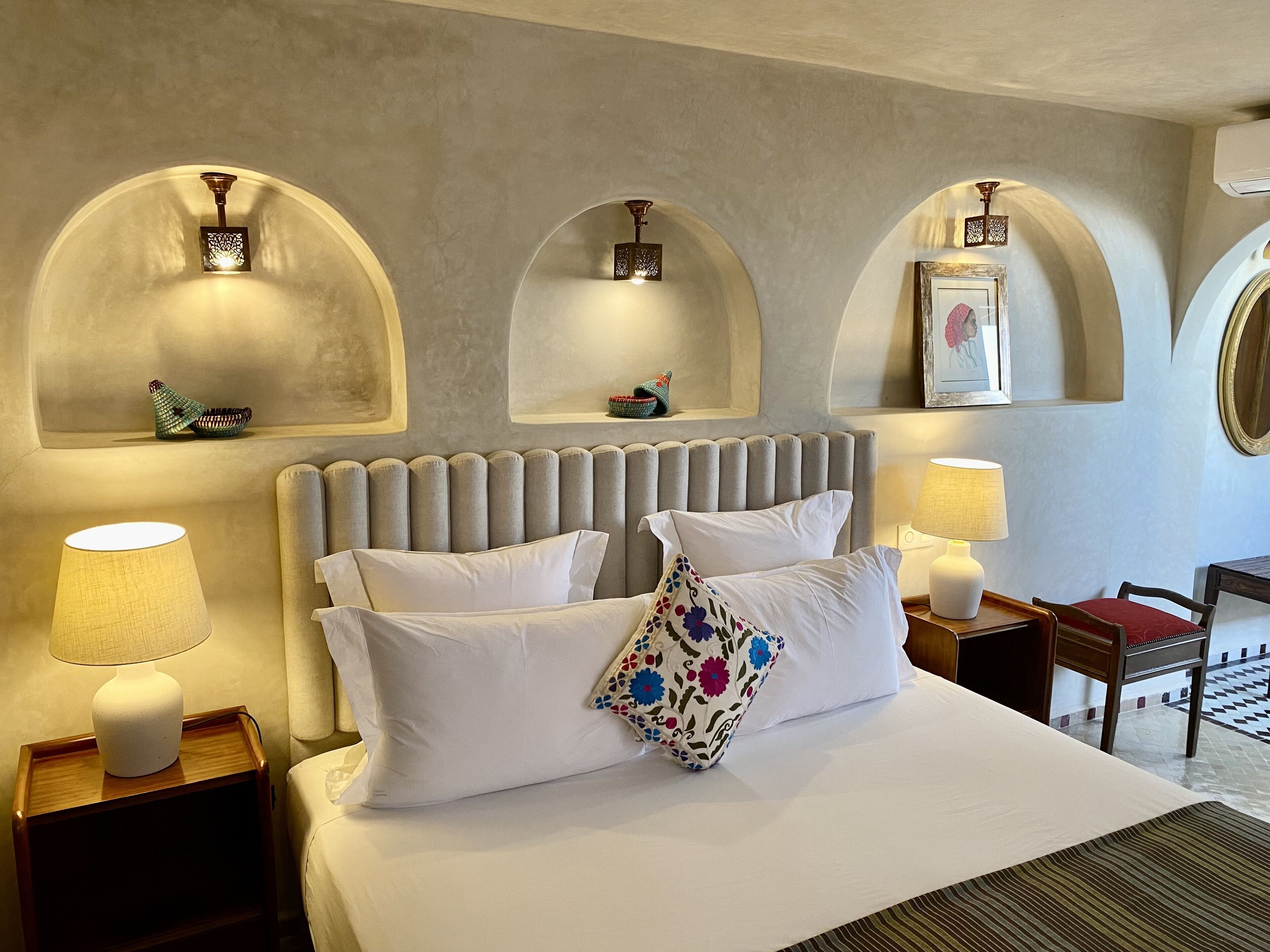 Hotelkamer met een groot bed, twee bedlampjes, een nachtkastje, een stoel en een klein tafeltje met lamp.