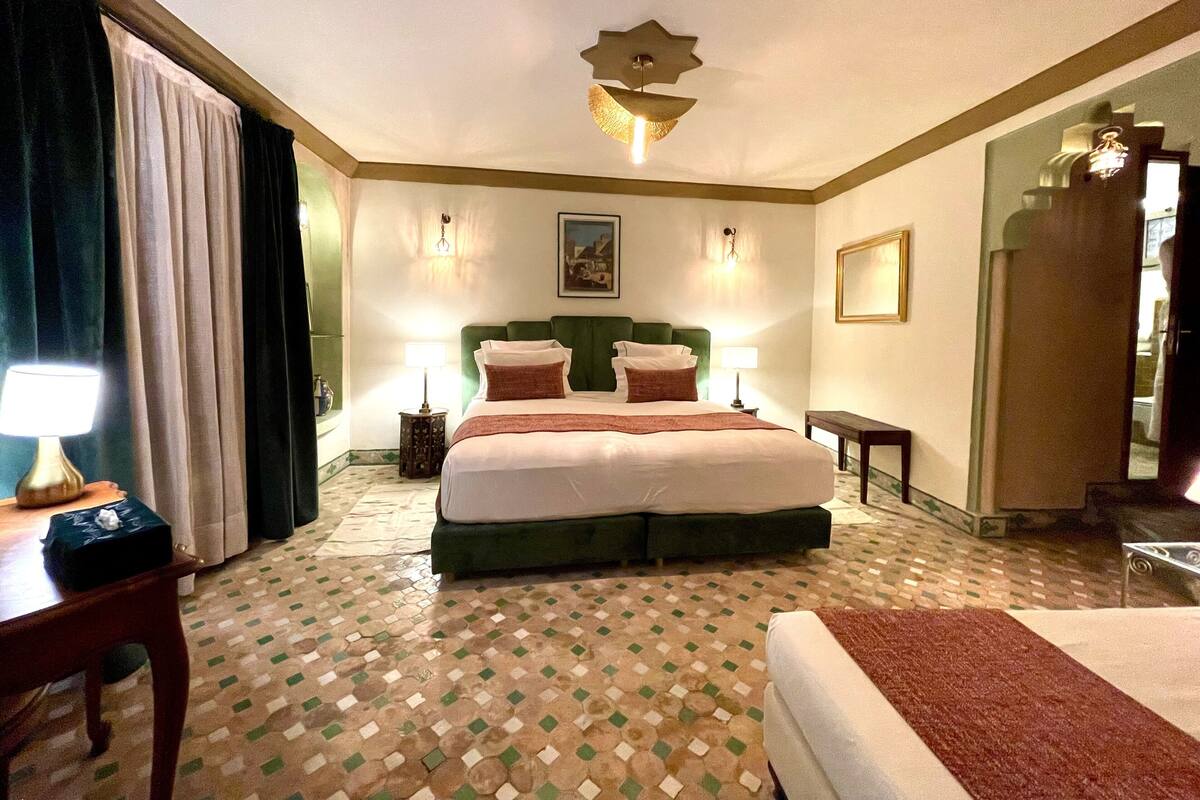 A hotel room with a large bed, two bedside lamps, a green headboard, a patterned floor, and a mirror on one wall.