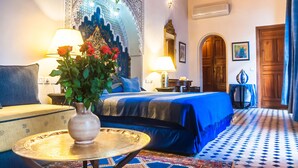 Habitación de hotel con cama, zona de estar con mesa y sillas, un tapiz decorativo y suelo estampado.