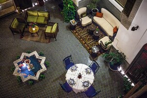 Ampla sala de estar com piso xadrez, uma mesa de jantar redonda com cadeiras e um conjunto de sofás.