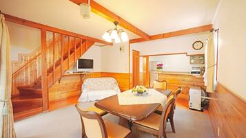 Une pièce chaleureuse avec un escalier en bois, un canapé, une table à manger avec des chaises, un petit coin cuisine et une horloge au mur.