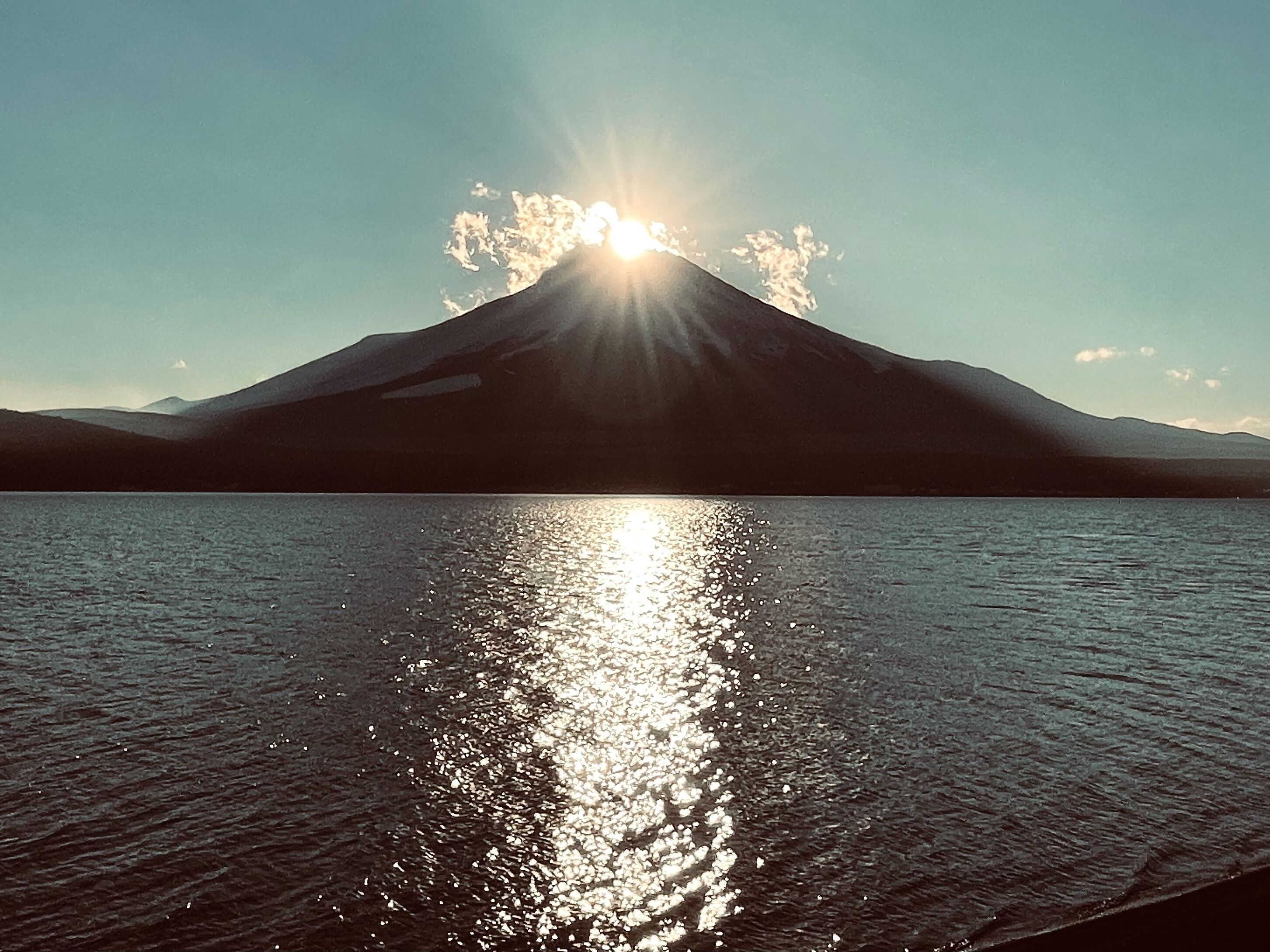 Una montaña con el reflejo del sol en aguas tranquilas.