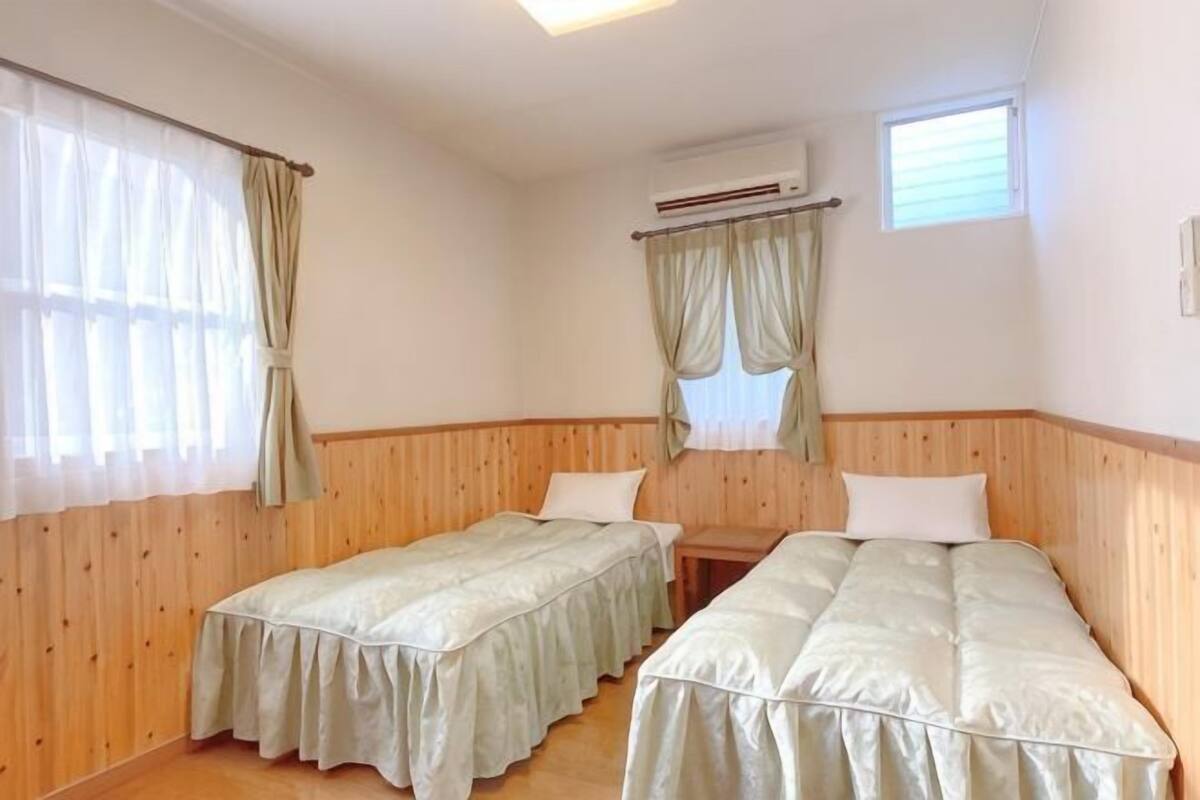 Une chambre avec deux lits, des lambris en bois, une fenêtre avec des rideaux et un appareil de climatisation.