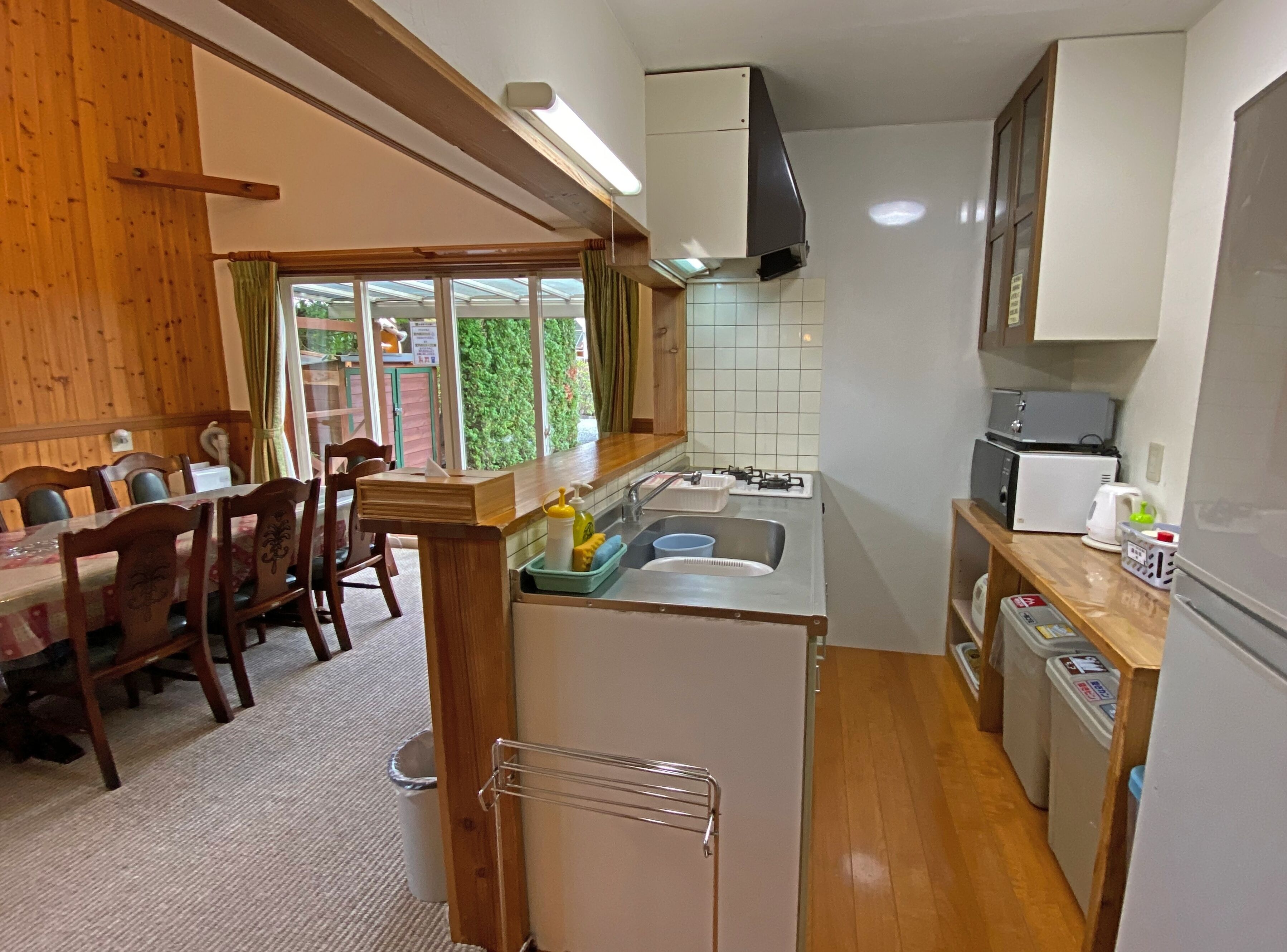 A compact kitchen with a sink, stove, and microwave. There is a dining area with wooden chairs and a table.