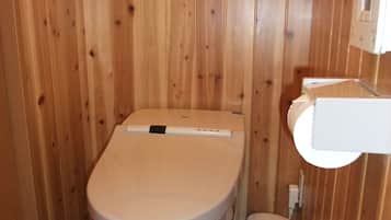 A small, wooden-paneled bathroom with a toilet, a bidet, and a shelf with toilet paper.