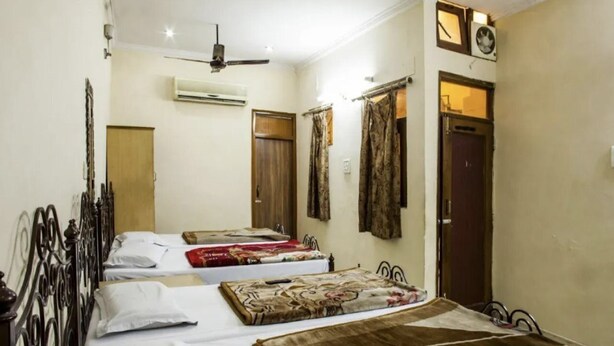 A room with three beds, a ceiling fan, an air conditioning unit, and a clock on the wall. - Roxy Dx (New Delhi)