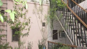 A building with a pink facade, a staircase with metal railings, and various plants around the exterior. - Roxy Dx (New Delhi)