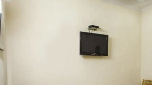A room with a mounted television on the wall, a ceiling fan, and a chair. - Roxy Dx (New Delhi)