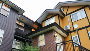 A multi-story residential building with a combination of siding and brickwork, featuring balconies and a satellite dish. - Pension Yama No Wagaya (Nasu)