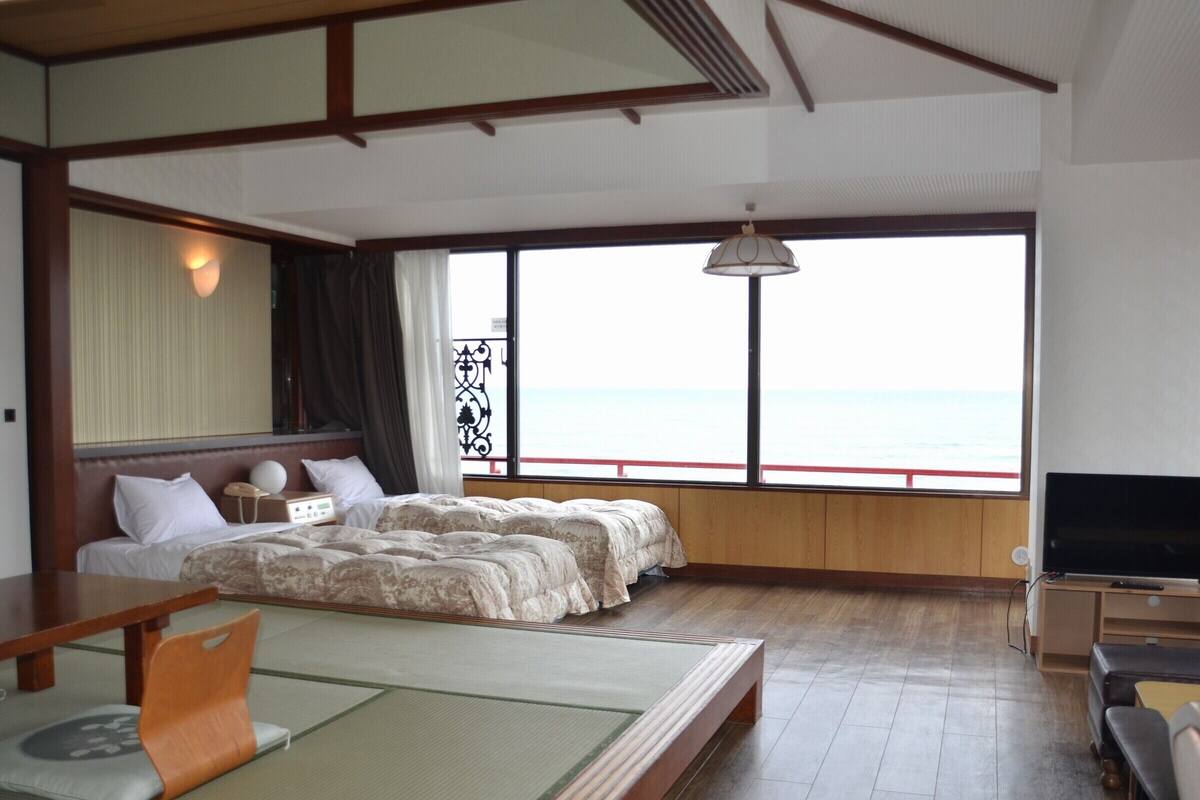 Una habitación con cama, televisión, mesa y vista al mar.