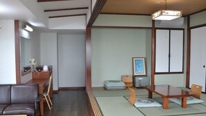 Una habitación tradicional japonesa con suelo de tatami, una mesa baja con cojines, un sofá y un armario con espejo.