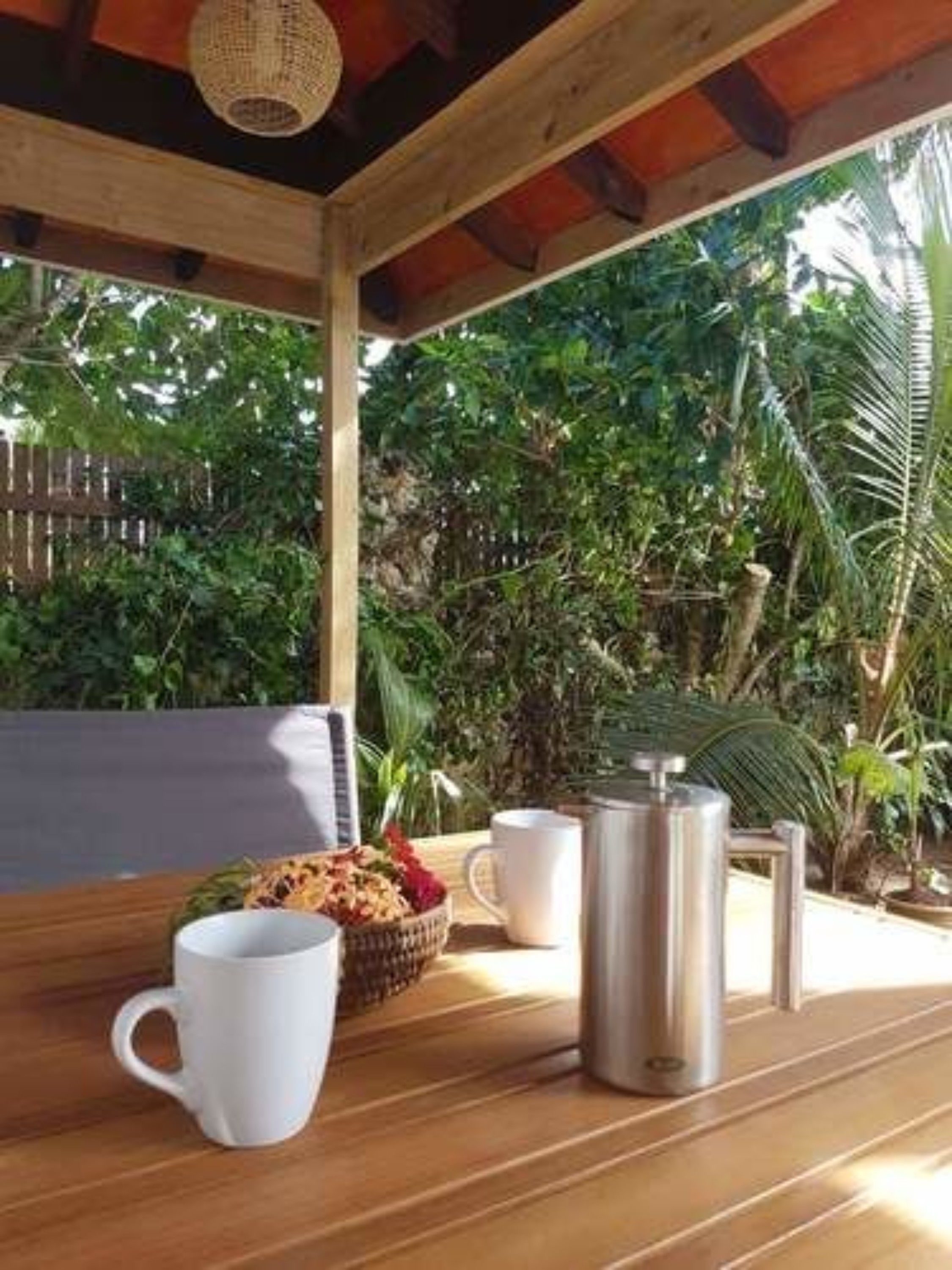 Een houten tafel met een witte mok, een roestvrijstalen koffiepot en een mand met fruit.