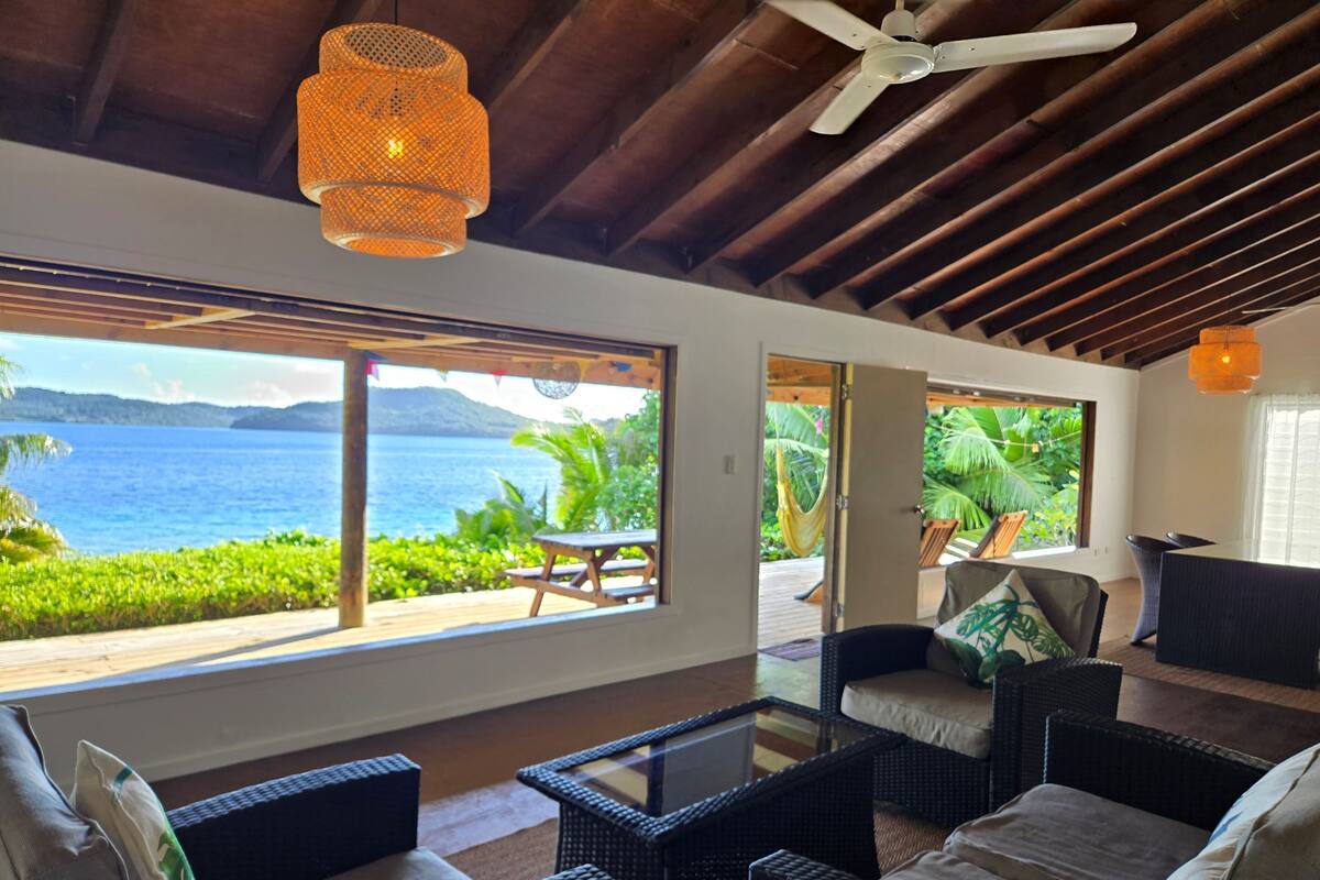 Una habitación con muebles de mimbre, ventilador de techo y vista al mar.