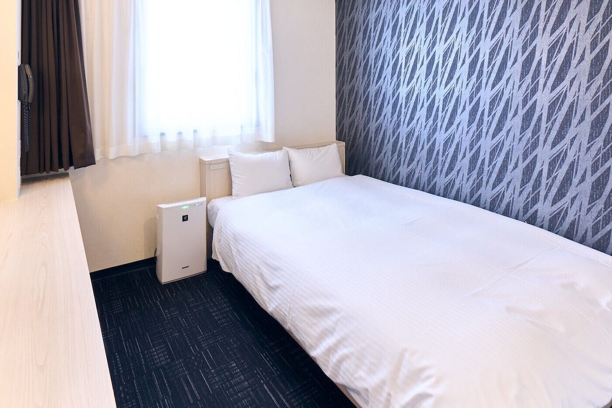 A hotel room with a bed, bedside table, lamp, and a small heater.