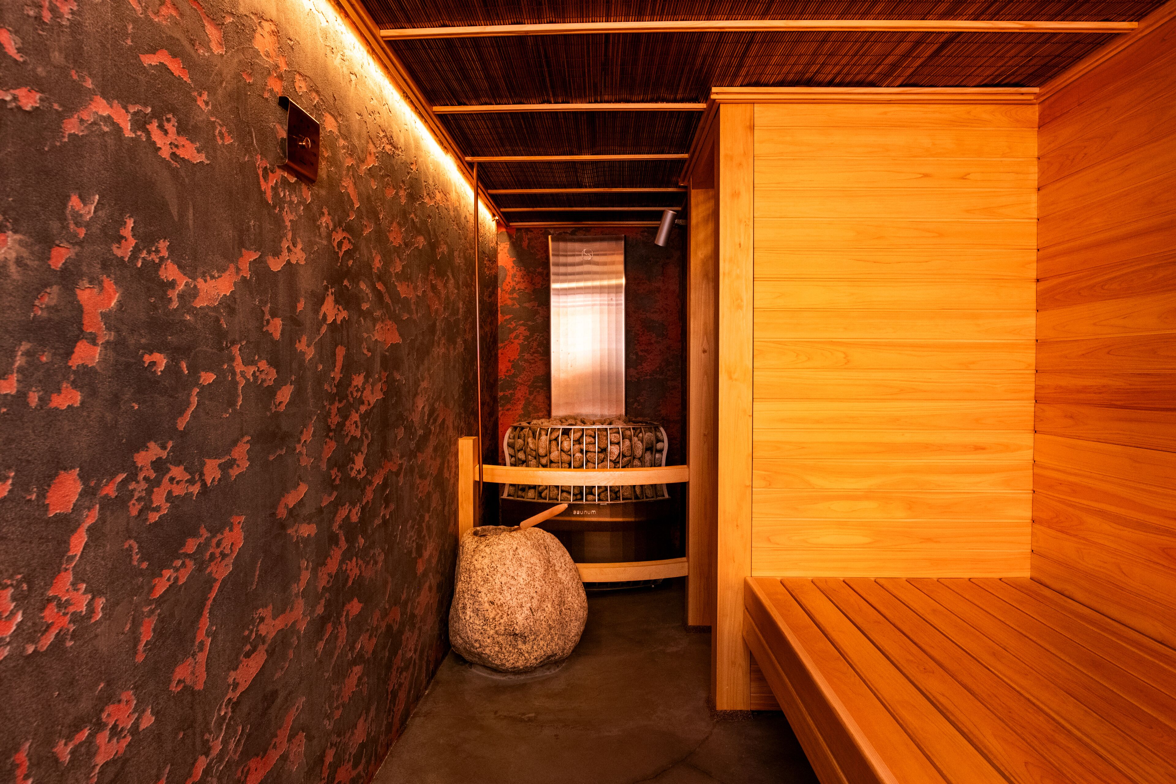 A sauna room with a bench, a stone seat, and a wooden wall.