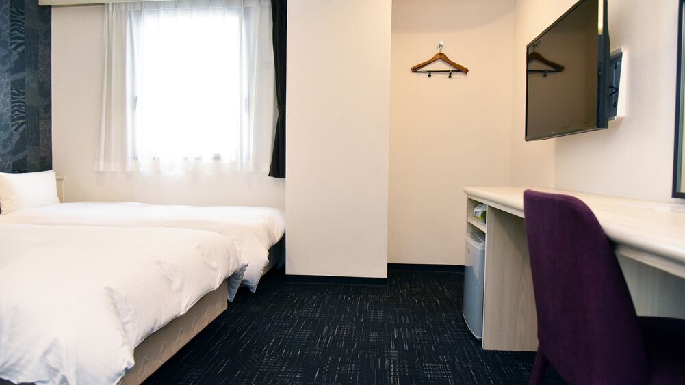A hotel room with two beds, a desk, a chair, a mirror, and a window with curtains.