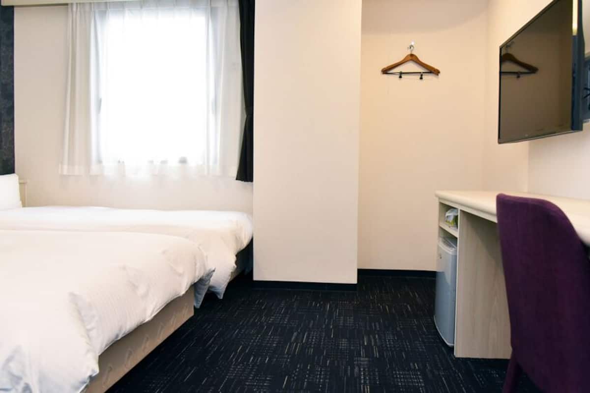 A hotel room with two beds, a desk, a chair, a mirror, and a window with curtains.
