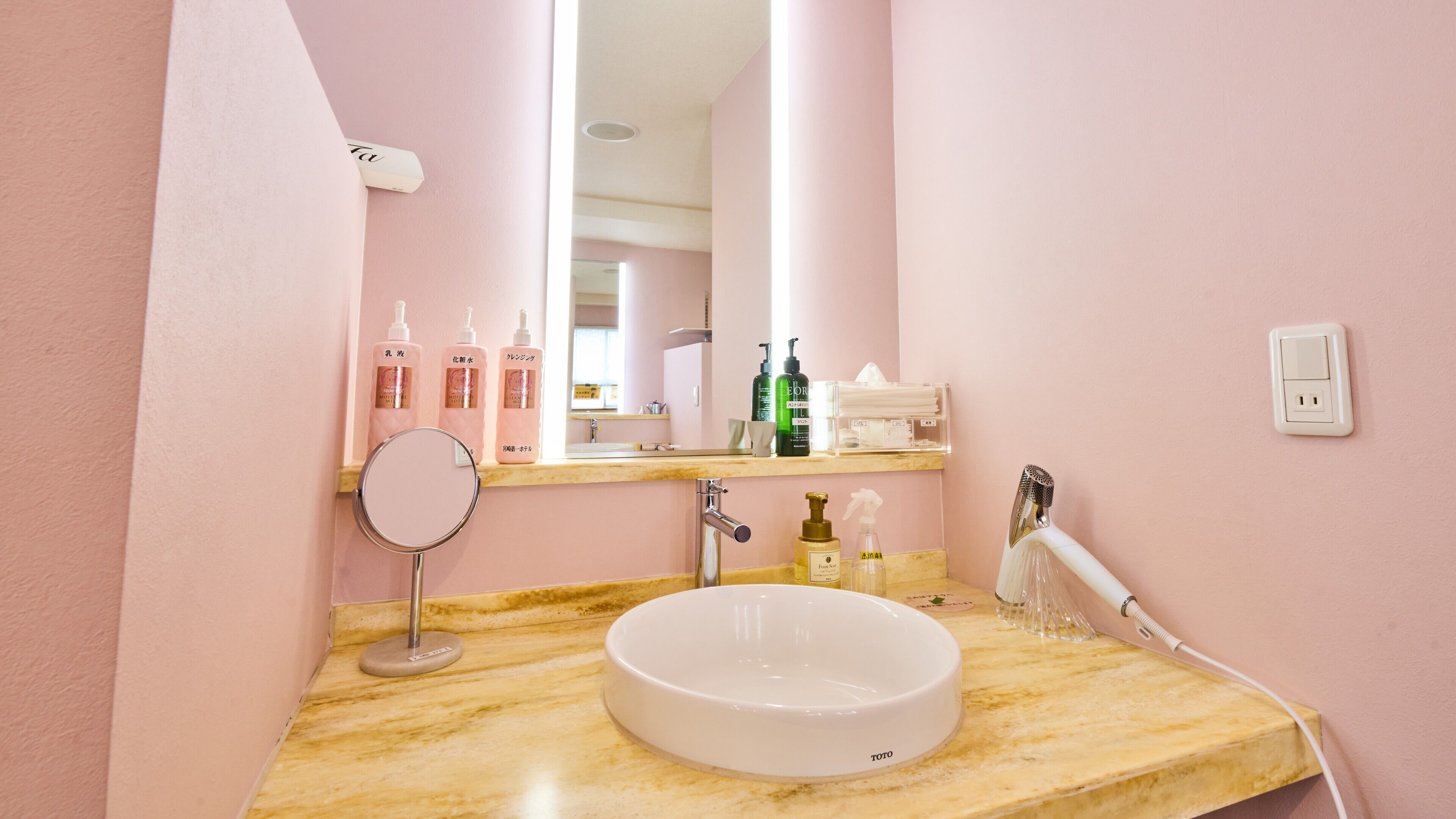 Une salle de bain avec un lavabo en marbre, un miroir, un sèche-cheveux et divers produits de toilette disposés sur le comptoir.