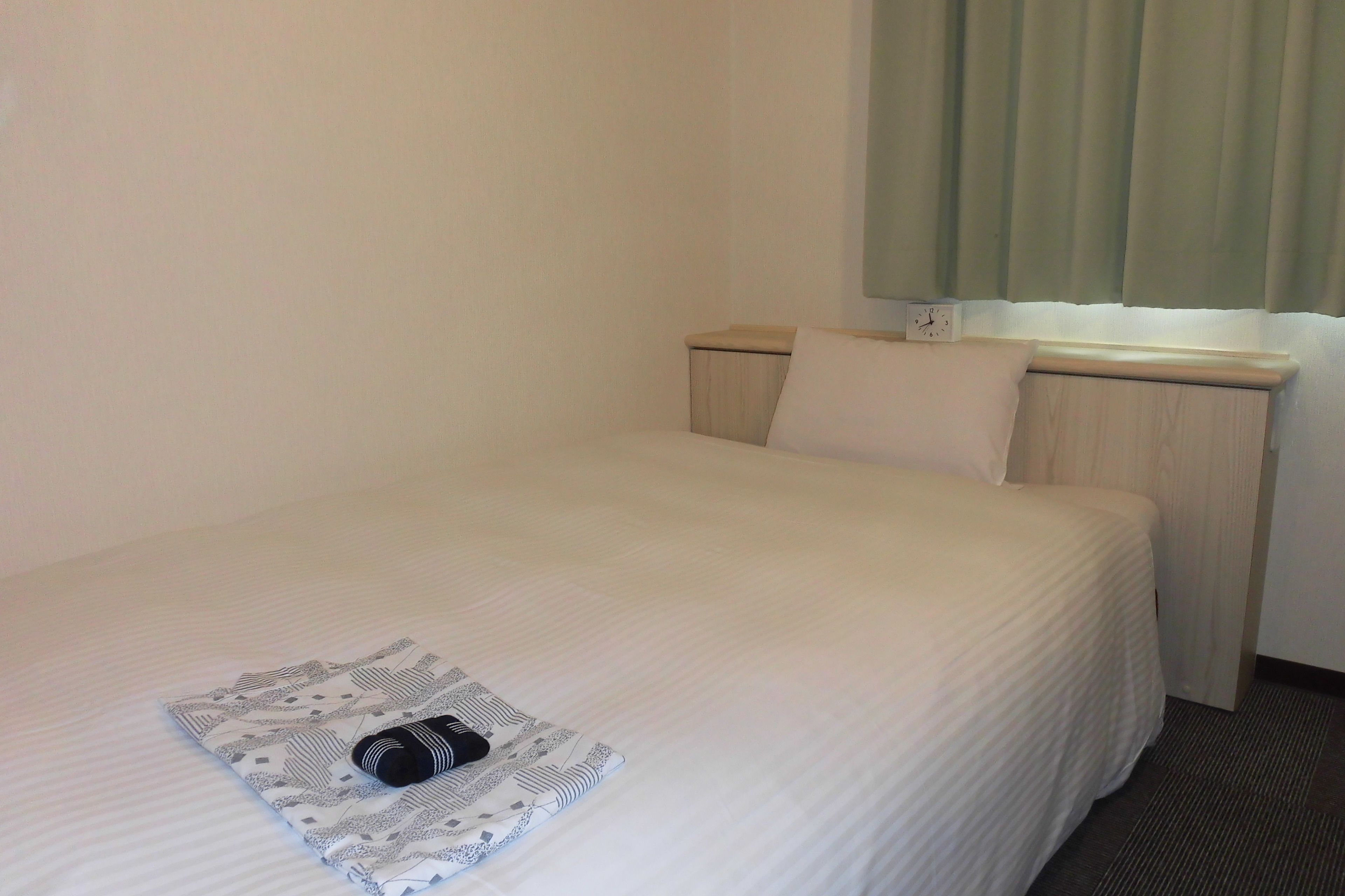 Cama arrumada com colcha branca e toalha dobrada estampada.